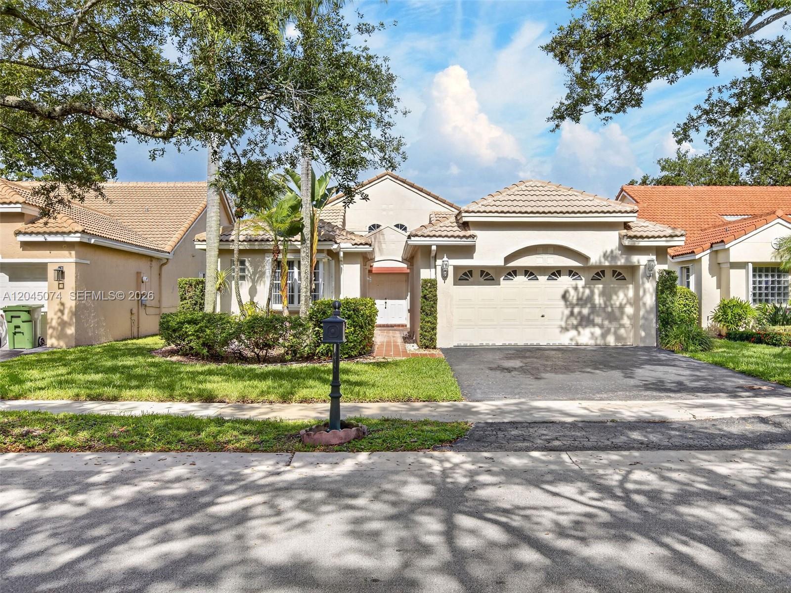 A single-story suburban house with a beige stucco exterior, tile roof, and two-car garage — 1520 Seabay Rd, Weston FL 33326, WESTON, FL