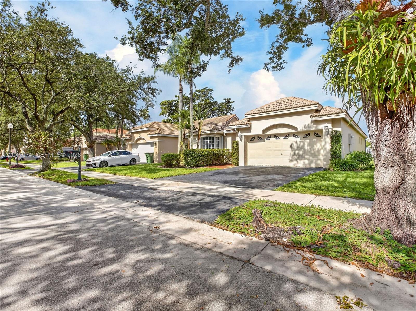 A street view of a suburban neighborhood featuring single-story houses with driveways and mature trees — 1520 Seabay Rd, Weston FL 33326, WESTON, FL