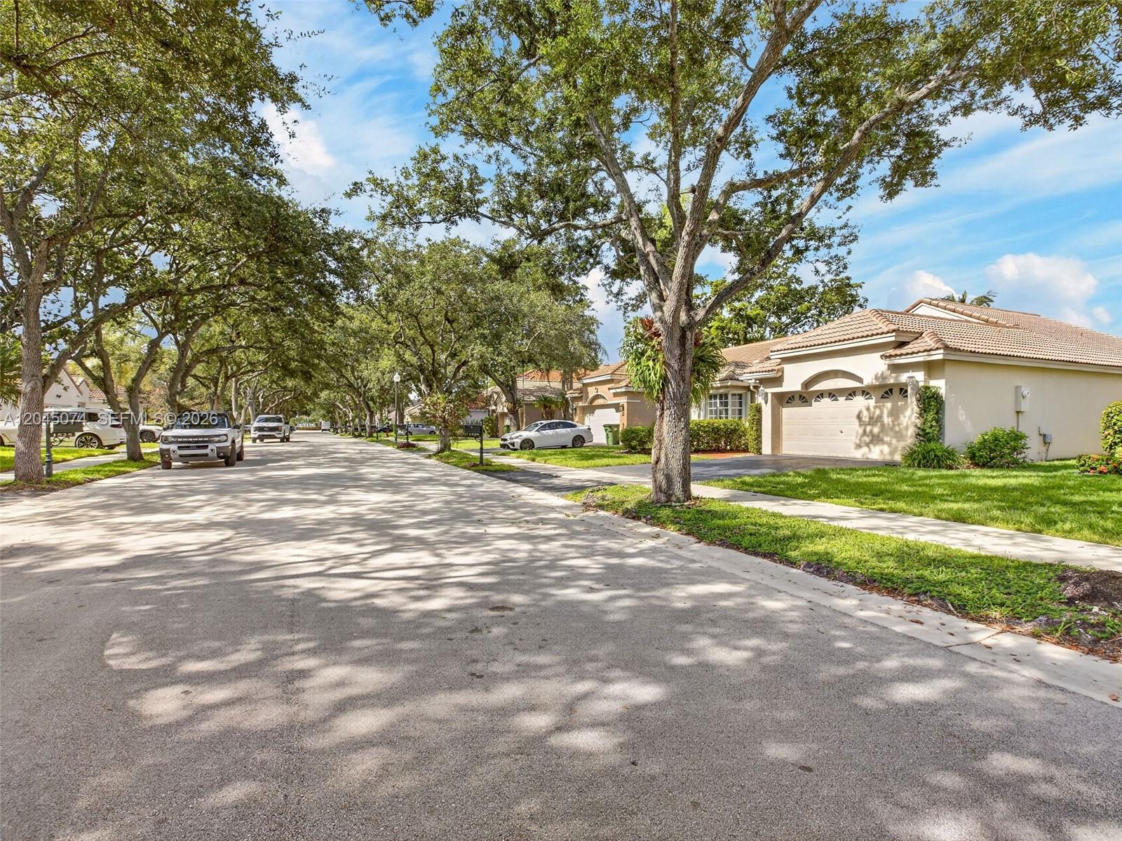 A quiet residential street lined with mature trees and single-story homes with attached garages — 1520 Seabay Rd, Weston FL 33326, WESTON, FL