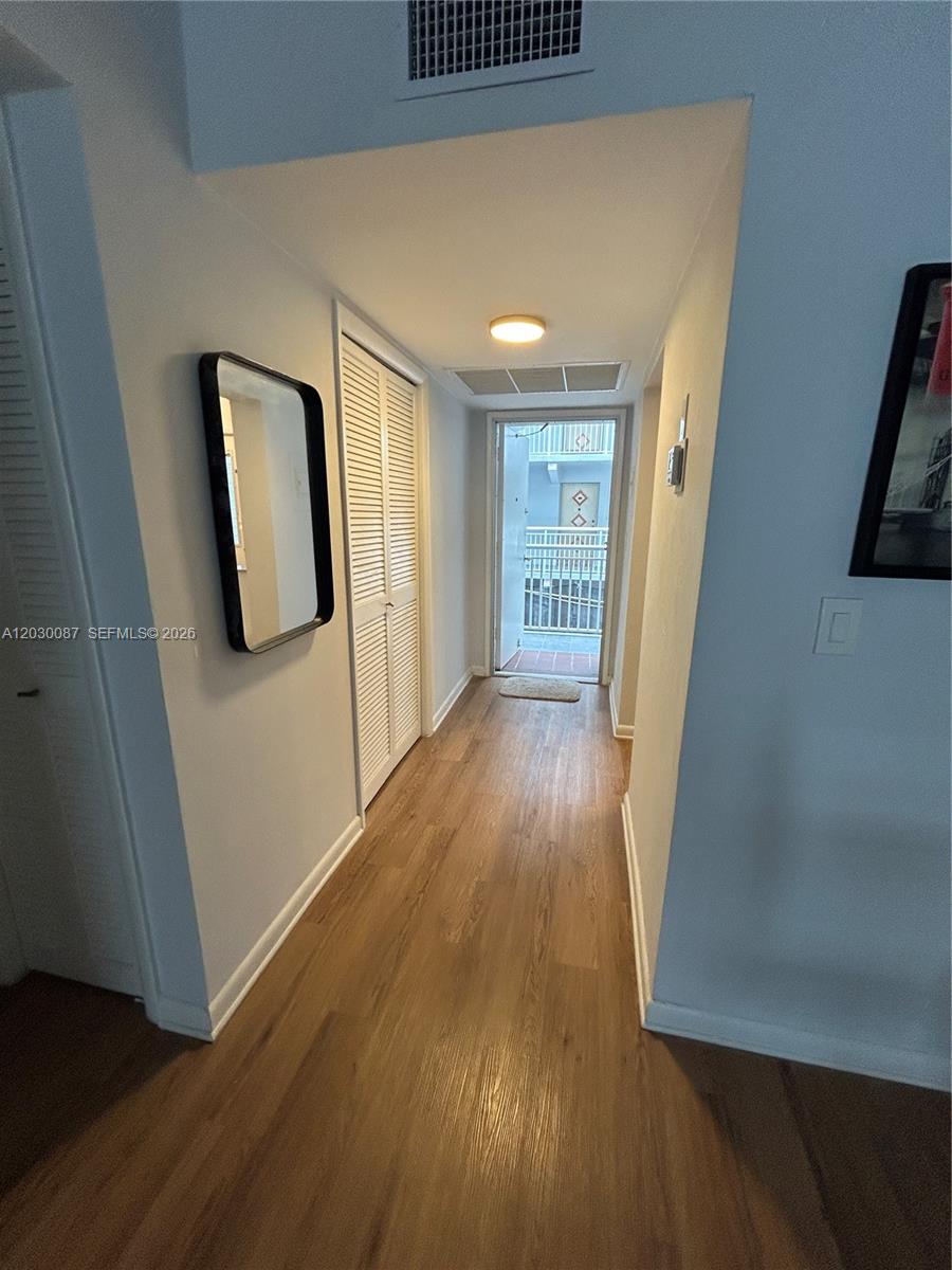 A hallway with light wood-look flooring leads to an exterior door with a metal railing — 215 SE 3rd Ave # 206A, Hallandale Beach FL 33009, HALLANDALE BEACH, FL