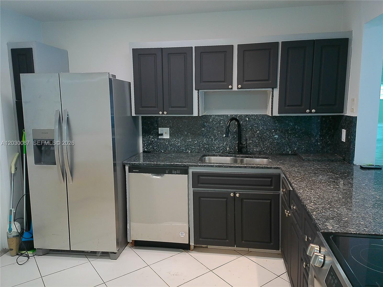 A kitchen features dark cabinets, granite countertops, stainless steel appliances, and white tile flooring — 215 SE 3rd Ave # 206A, Hallandale Beach FL 33009, HALLANDALE BEACH, FL