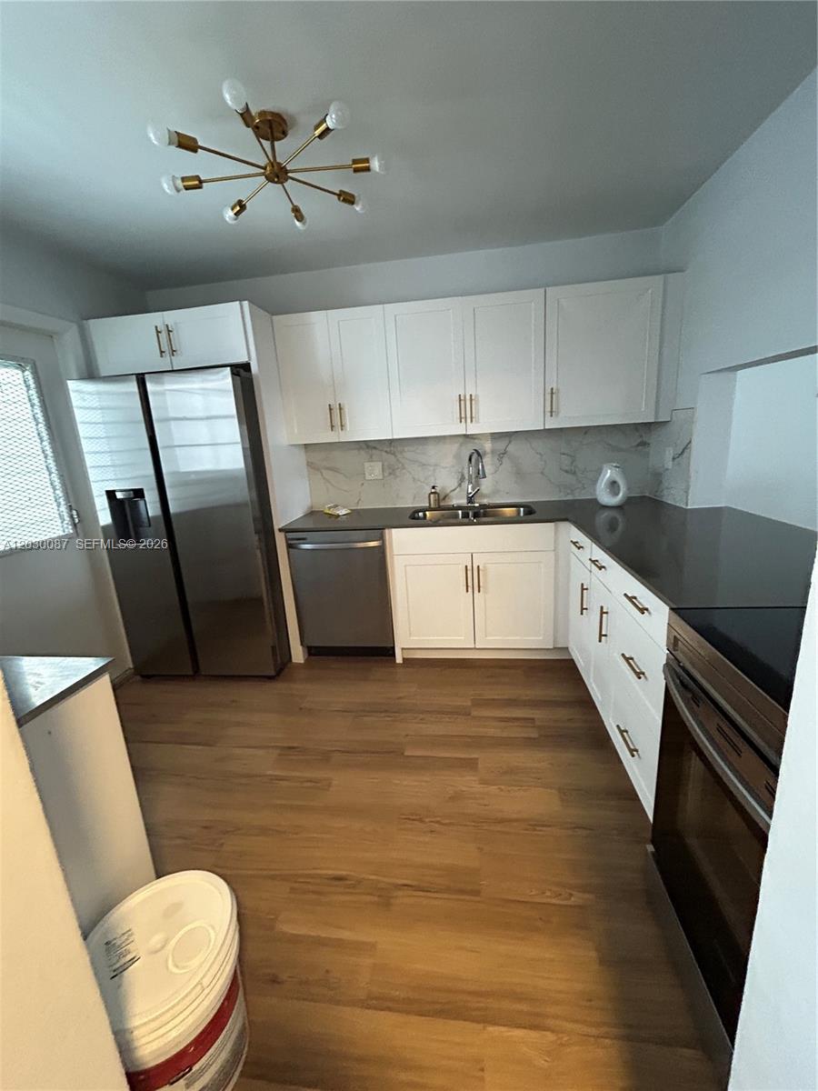 A kitchen features white cabinets, stainless steel appliances, dark countertops, and light wood flooring — 215 SE 3rd Ave # 206A, Hallandale Beach FL 33009, HALLANDALE BEACH, FL