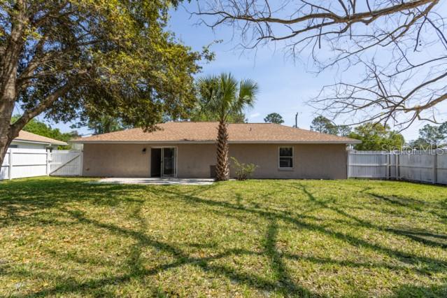The backyard of a single-story house features a palm tree, a patio, and white fencing — 3 PINE HAVEN DRIVE, PALM COAST, FL