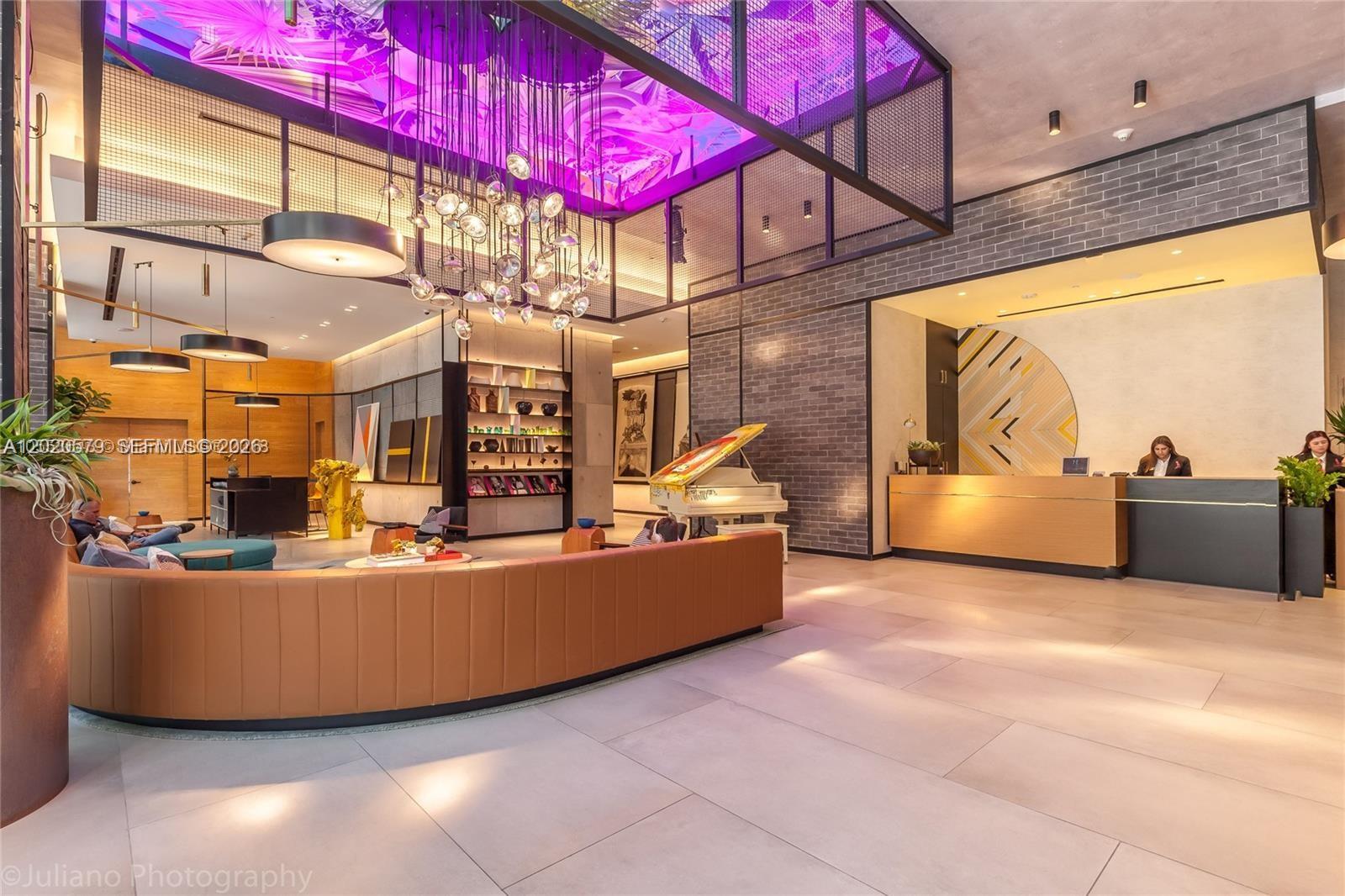 A modern hotel lobby features a curved leather sofa, a grand piano, and decorative lighting — 121 NE 34th St # 1007, Miami FL 33137, MIAMI, FL