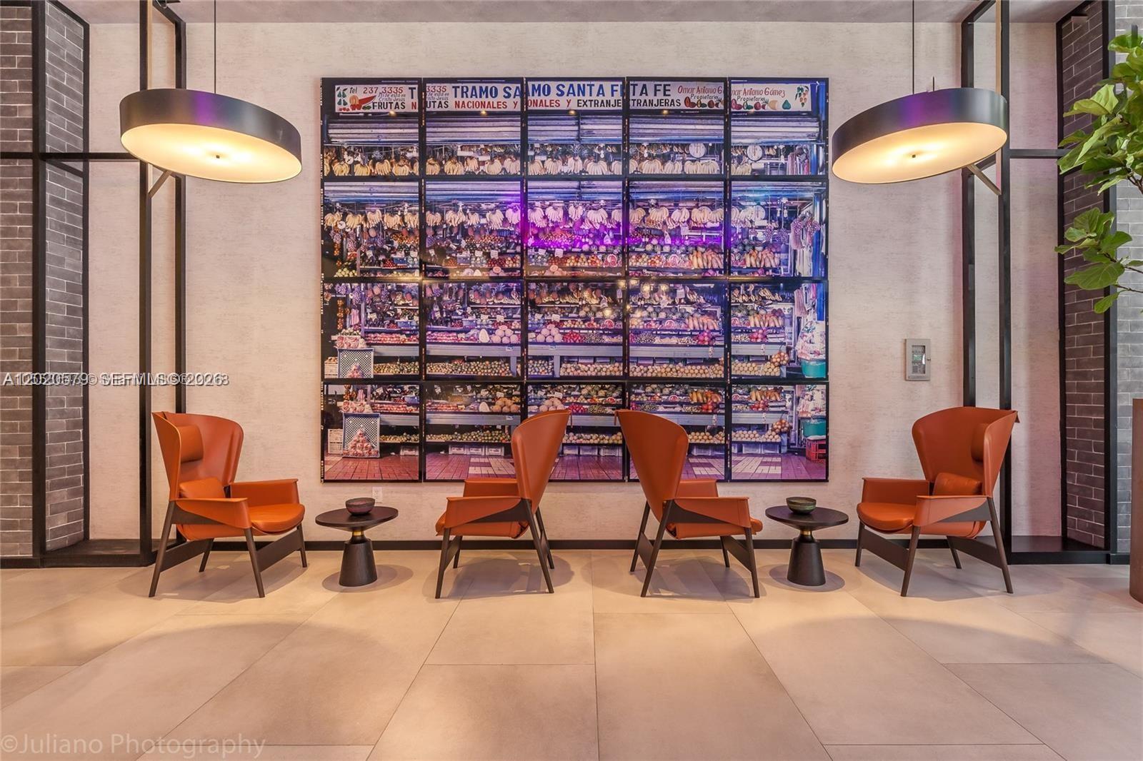 A modern lobby features four orange armchairs, two side tables, and a large fruit-stand mural — 121 NE 34th St # 1007, Miami FL 33137, MIAMI, FL