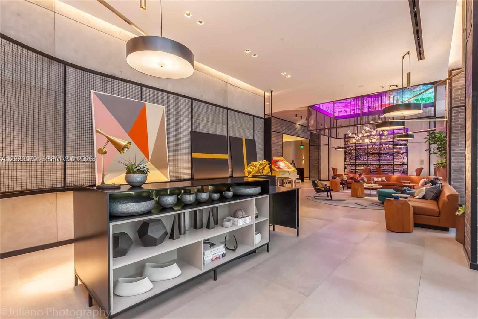 A modern lobby features a black shelving unit, abstract artwork, and a spacious seating area — 121 NE 34th St # 1007, Miami FL 33137, MIAMI, FL