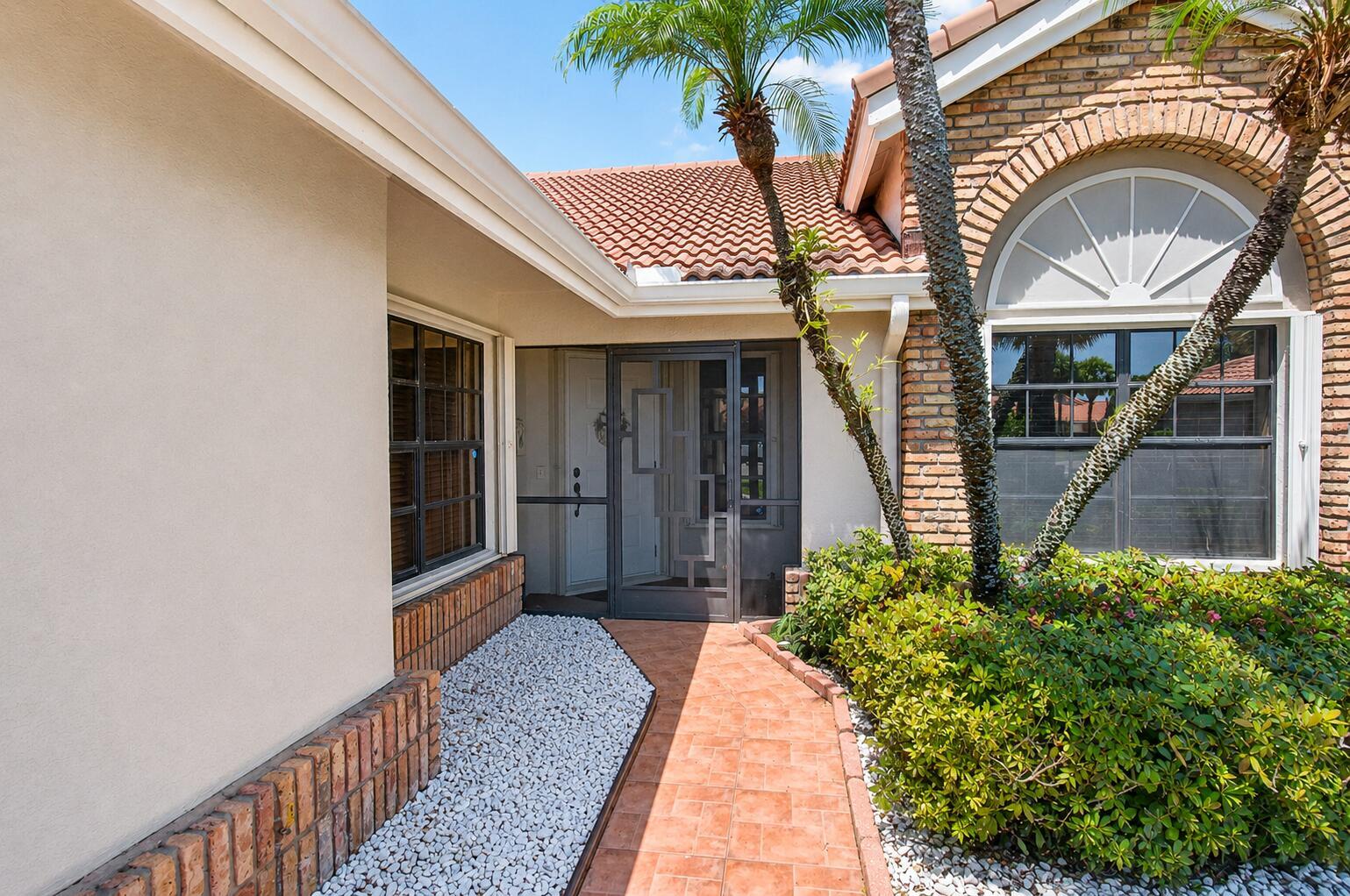 A tiled walkway leads to a screened front door flanked by brick and stucco walls — 7481 Hearth Stone Avenue, Boynton Beach FL 33472, BOYNTON BEACH, FL