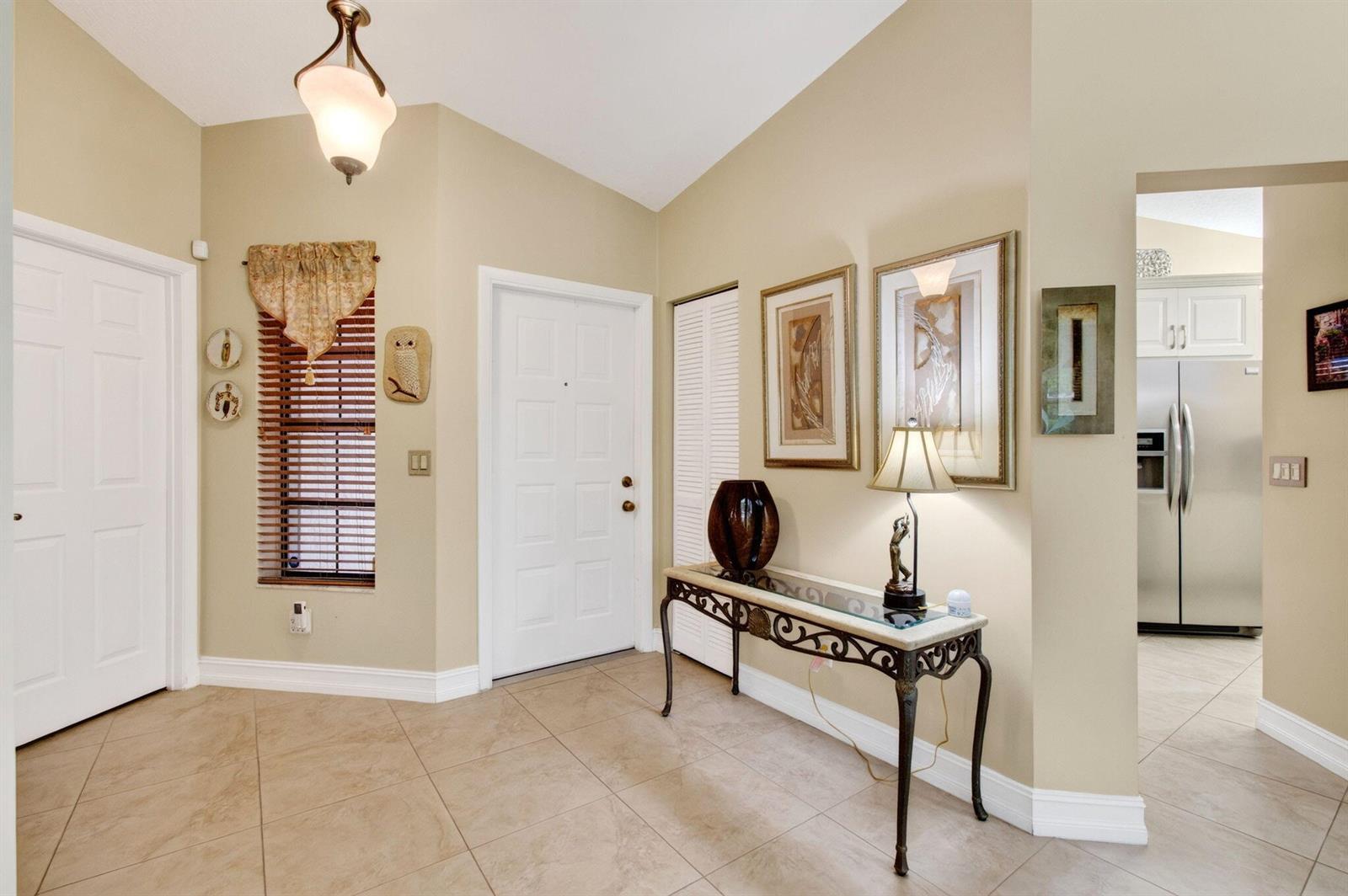 An entryway features beige tile floors, a console table, wall art, and a white door — 7481 Hearth Stone Avenue, Boynton Beach FL 33472, BOYNTON BEACH, FL