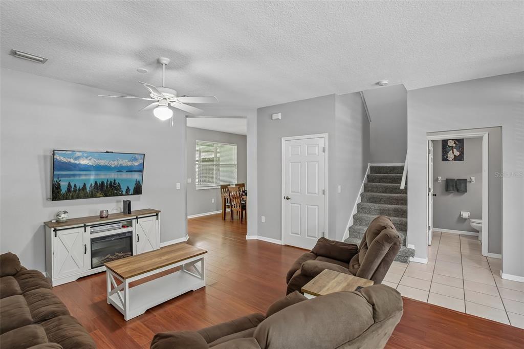 A living room features wood flooring, a television console, brown furniture, and a staircase — 34842 TEEVIEW LANE, ZEPHYRHILLS, FL