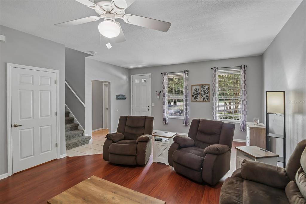 A living room features brown recliners, wood-look flooring, a ceiling fan, and a staircase — 34842 TEEVIEW LANE, ZEPHYRHILLS, FL
