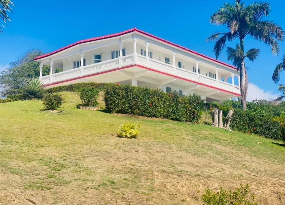 A white two-story house with a red roof and a wraparound balcony sits on a hill — 901 AMAZING VIEW HOUSE, MAUNABO, PR
