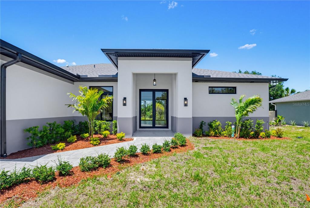 The exterior of a modern house features a covered entryway, glass doors, and landscaped gardens — 5073 HIGHTOWER ROAD, NORTH PORT, FL