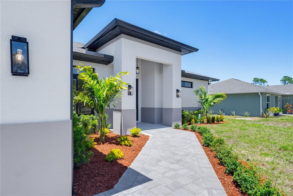 A modern house exterior features a paved walkway leading to a covered entryway — 5073 HIGHTOWER ROAD, NORTH PORT, FL