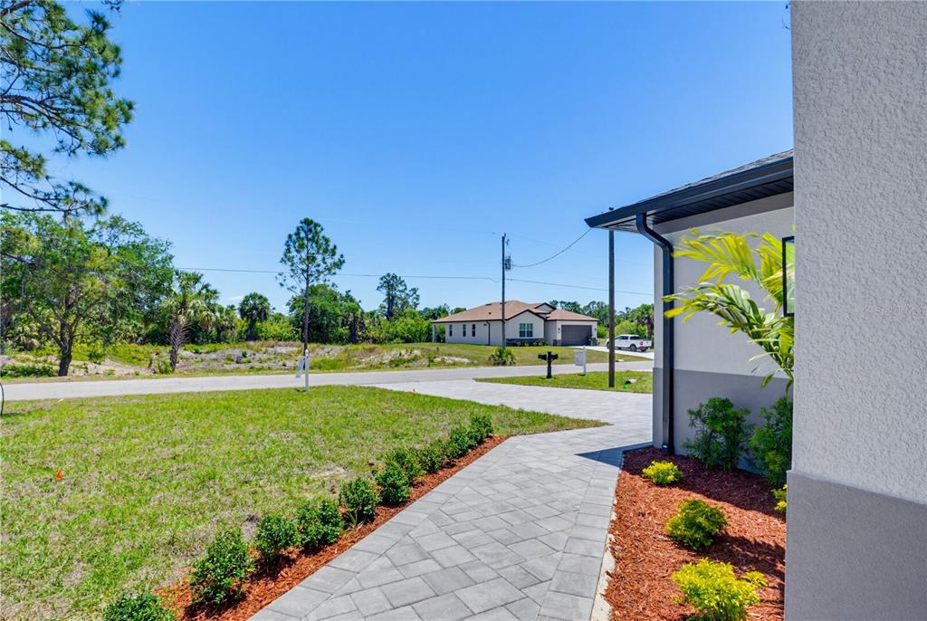 A paved walkway leads toward a house exterior with a lawn and surrounding trees — 5073 HIGHTOWER ROAD, NORTH PORT, FL