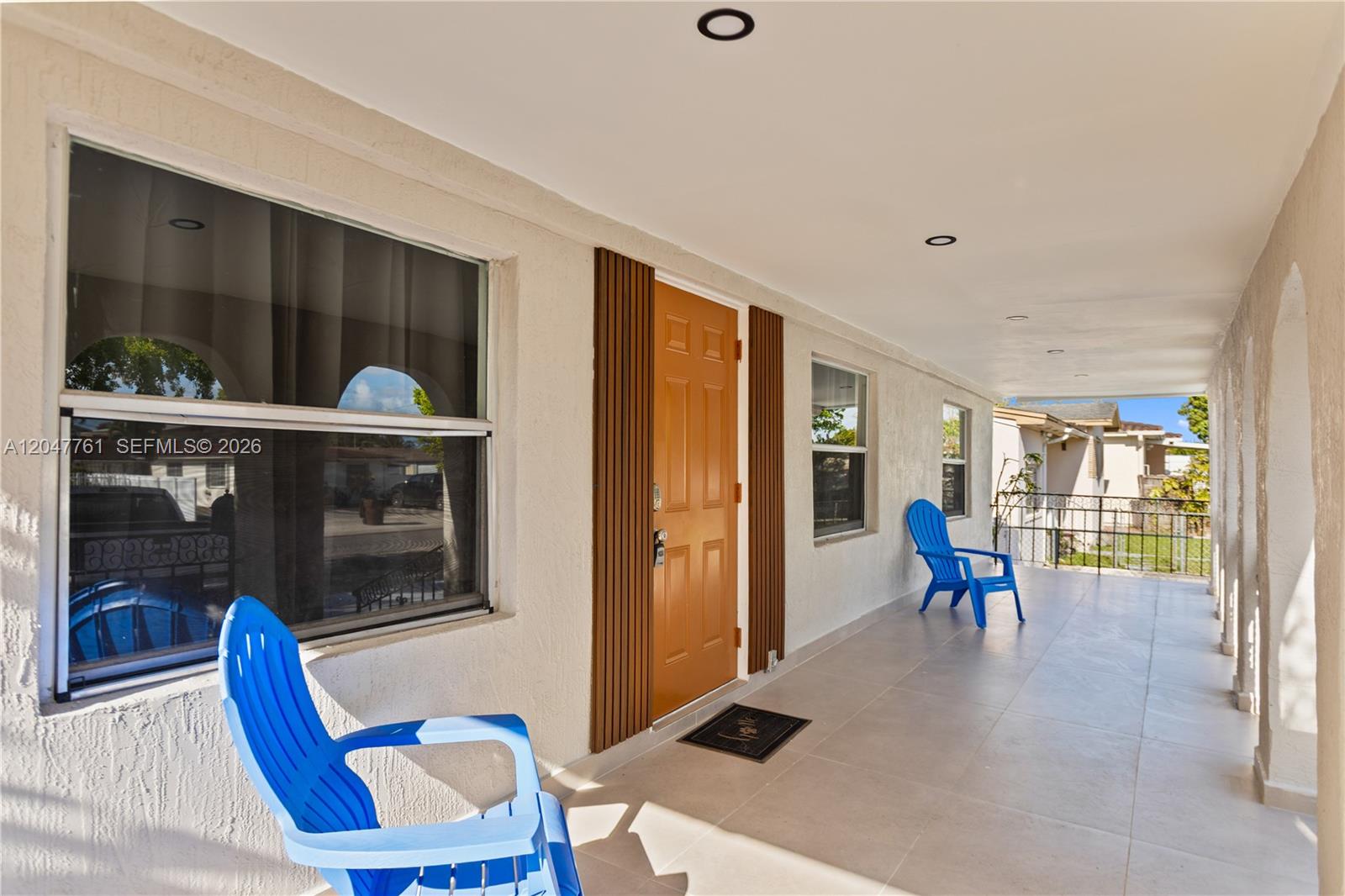 A covered porch features light-colored tile flooring, a tan door, and two bright blue chairs — 171 W 13th St # 171, Hialeah FL 33010, HIALEAH, FL