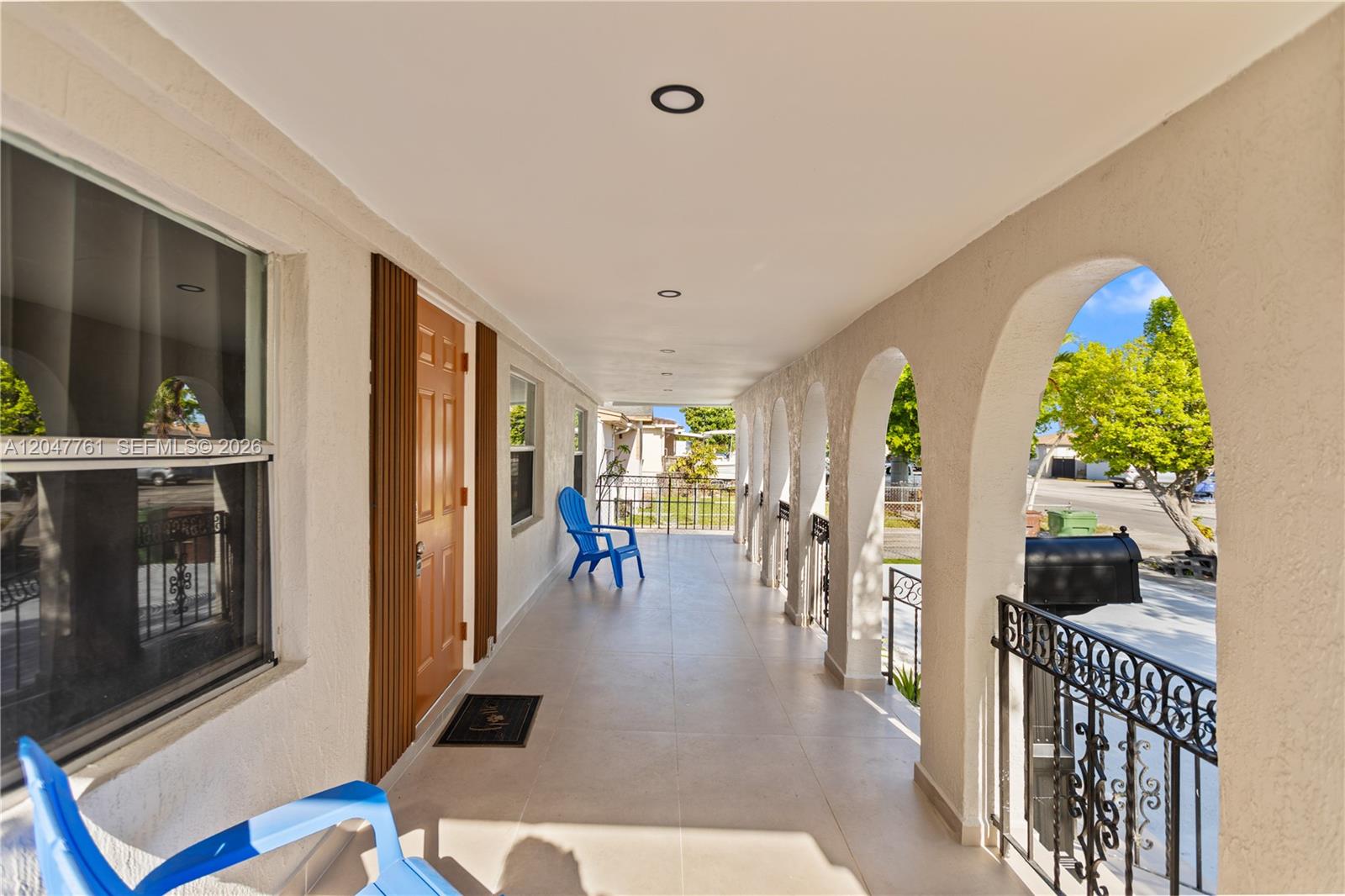 A covered porch features arched openings, tiled flooring, and blue chairs along the exterior wall — 171 W 13th St # 171, Hialeah FL 33010, HIALEAH, FL