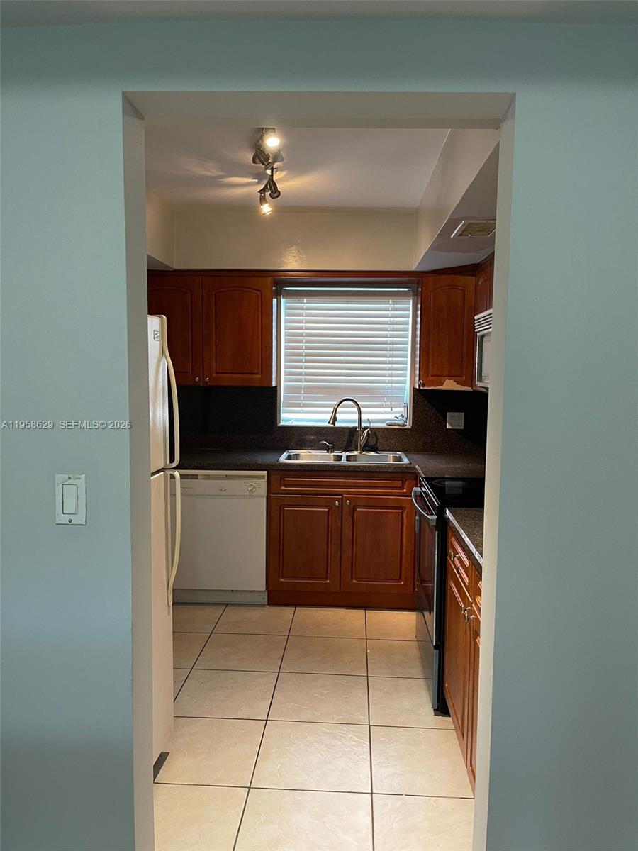 A galley kitchen features wood cabinets, dark countertops, a white dishwasher, and tile flooring — 7670 SW 82nd St # H113, Miami FL 33143, MIAMI, FL