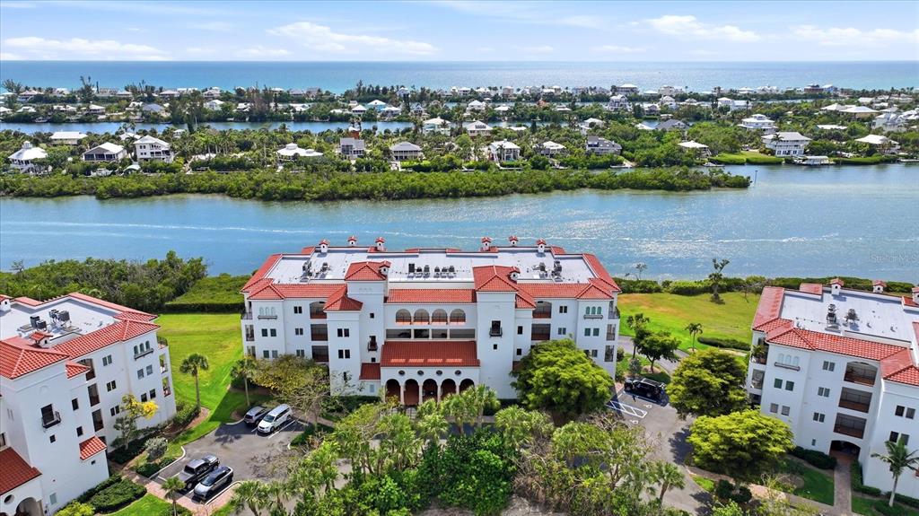 An aerial view shows three multi-story white buildings with red tile roofs near a waterway — 11160 HACIENDA DEL MAR BOULEVARD UNIT 202, PLACIDA, FL
