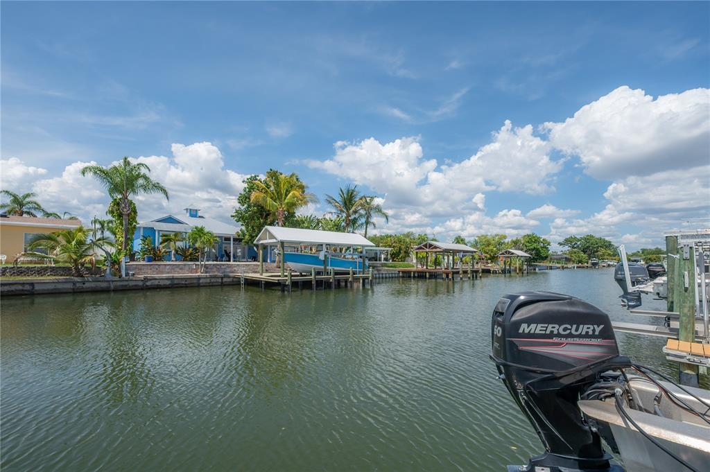 A canal view features a boat lift, a dock, and a house with palm trees — 8757 BAY POINTE DRIVE, TAMPA, FL