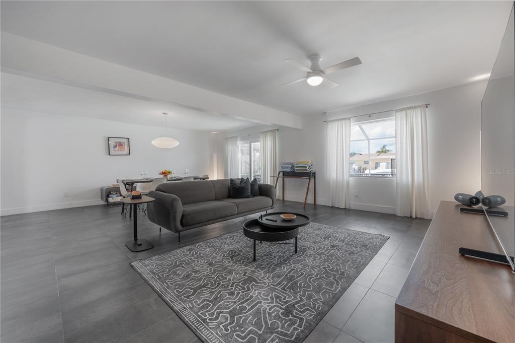 A living room with gray tile floors, a dark sofa, and a patterned area rug — 8757 BAY POINTE DRIVE, TAMPA, FL