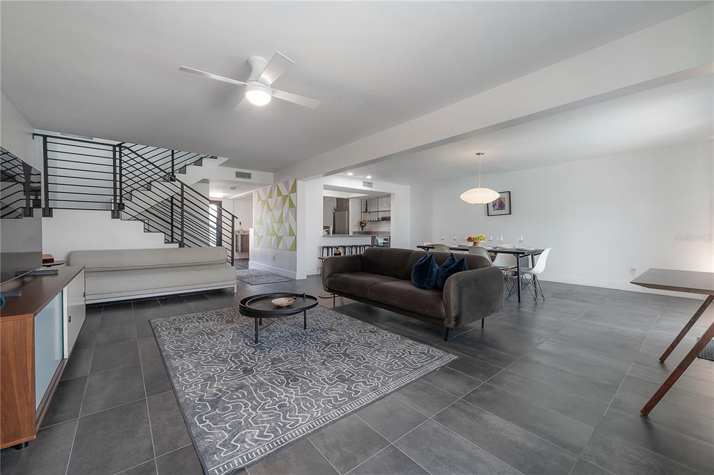 An open-concept living and dining area features gray tile floors, a staircase, and modern furnishings — 8757 BAY POINTE DRIVE, TAMPA, FL