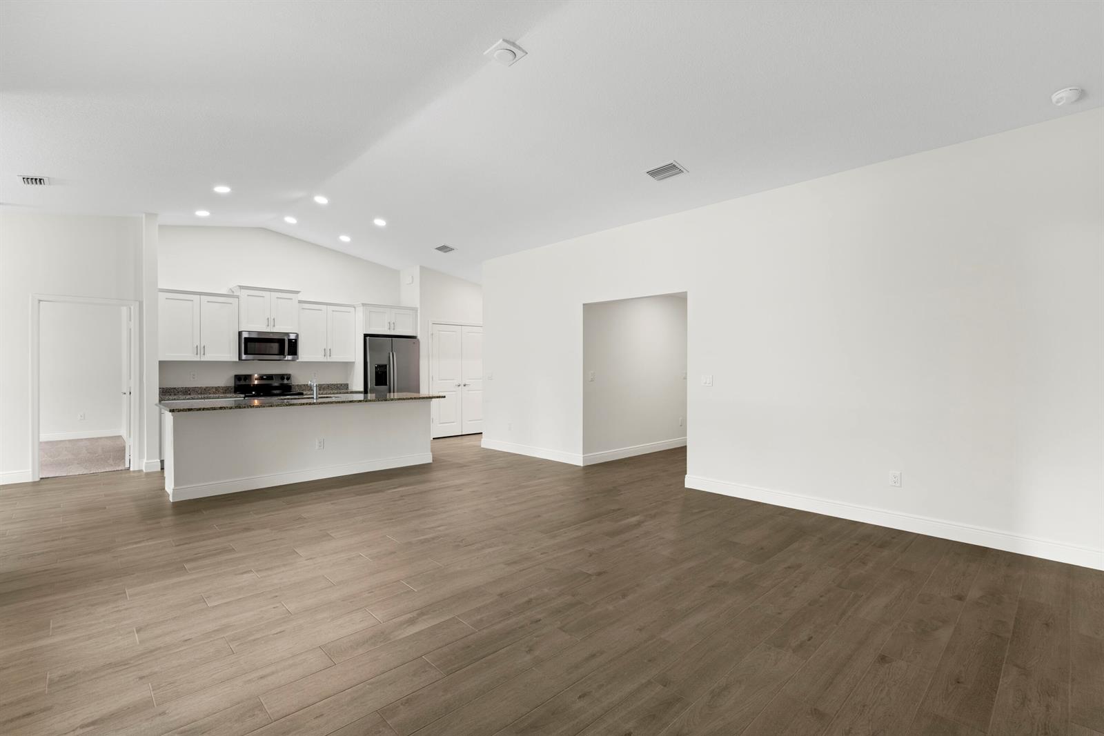 A kitchen with white cabinets and a granite island opens into a large living area — 15577 83rd Lane N, Loxahatchee FL 33470, LOXAHATCHEE, FL