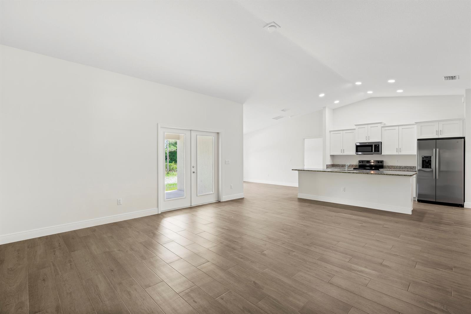 An open-concept living area features light wood-look tile flooring, white walls, and a modern kitchen — 15577 83rd Lane N, Loxahatchee FL 33470, LOXAHATCHEE, FL