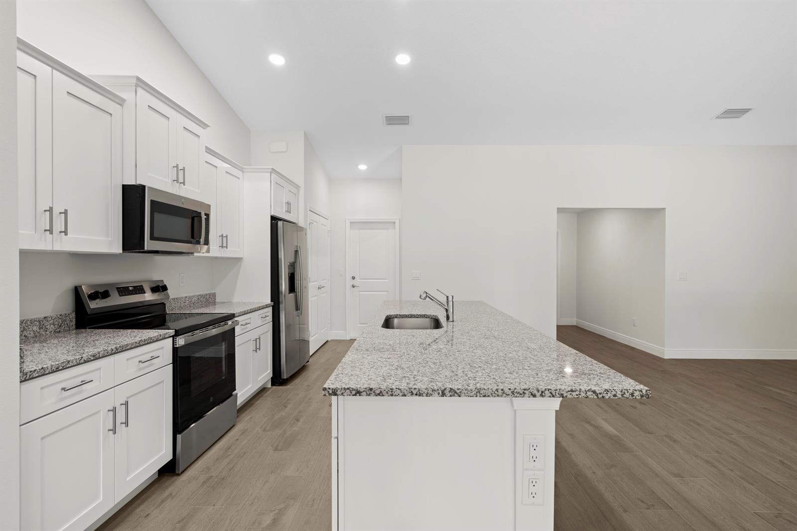 A modern kitchen features white cabinets, granite countertops, stainless steel appliances, and wood-look flooring — 15577 83rd Lane N, Loxahatchee FL 33470, LOXAHATCHEE, FL