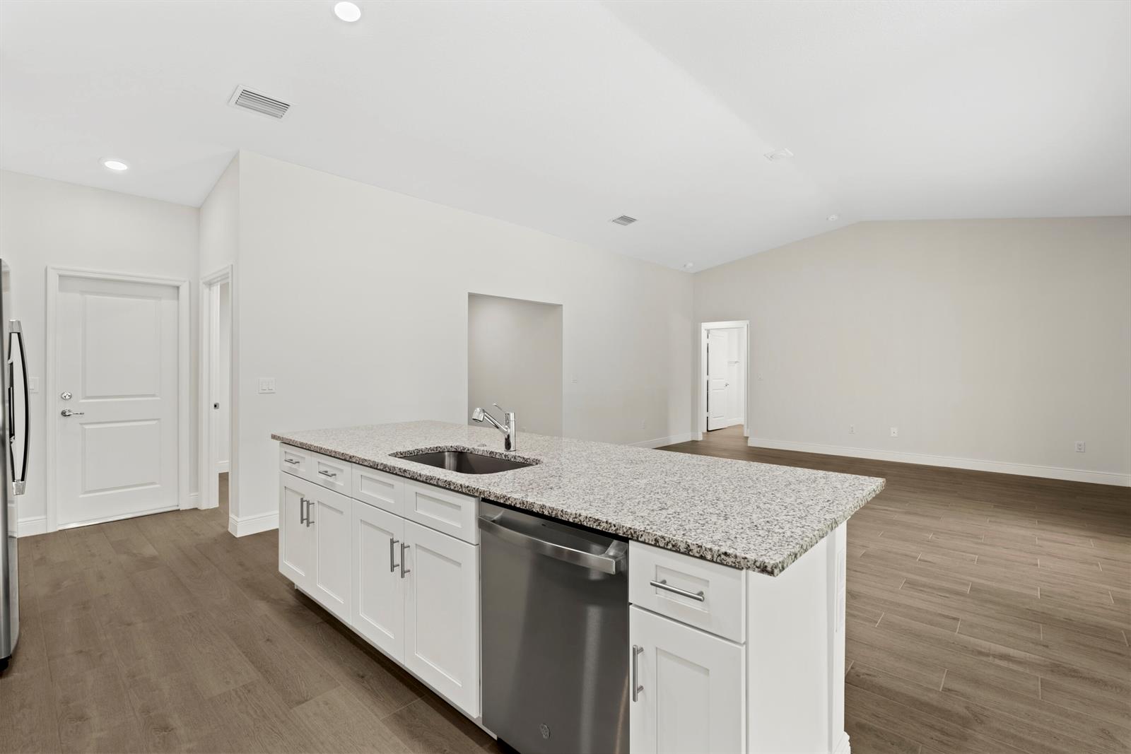 A kitchen island with a granite countertop and stainless steel dishwasher sits in an open room — 15577 83rd Lane N, Loxahatchee FL 33470, LOXAHATCHEE, FL