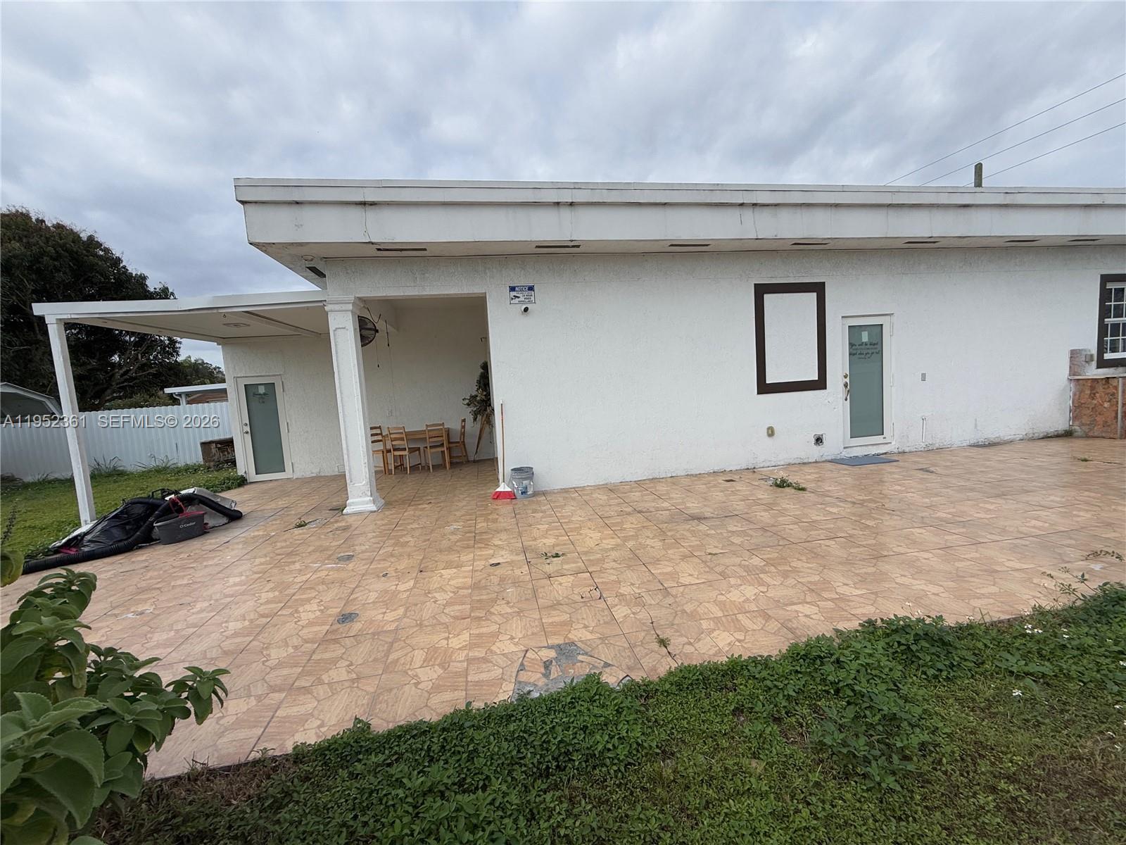 A white building features a tiled patio, a covered seating area, and two glass doors — 12202 SW 216th St, Miami FL 33170, MIAMI, FL