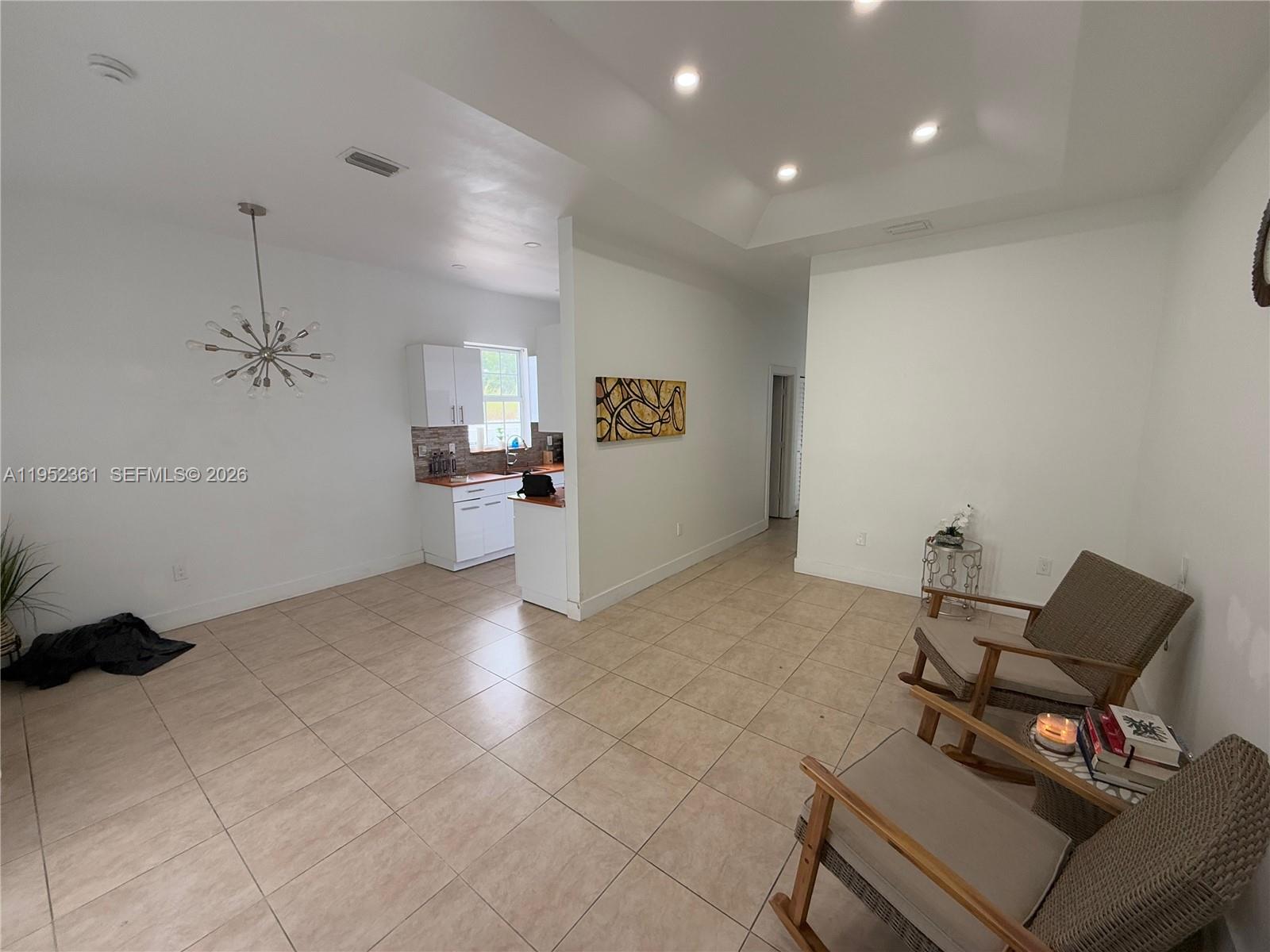An open-concept room features tiled floors, white walls, a kitchen area, and two rocking chairs — 12202 SW 216th St, Miami FL 33170, MIAMI, FL