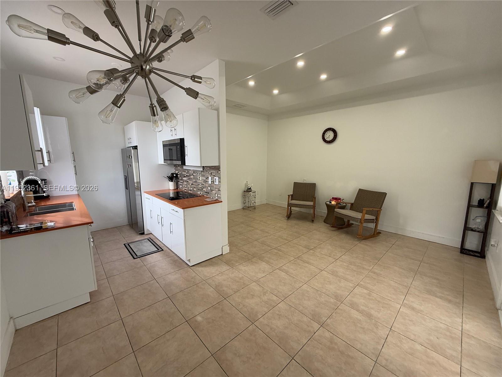 A kitchen with white cabinets and wood countertops opens into a spacious tiled living area — 12202 SW 216th St, Miami FL 33170, MIAMI, FL