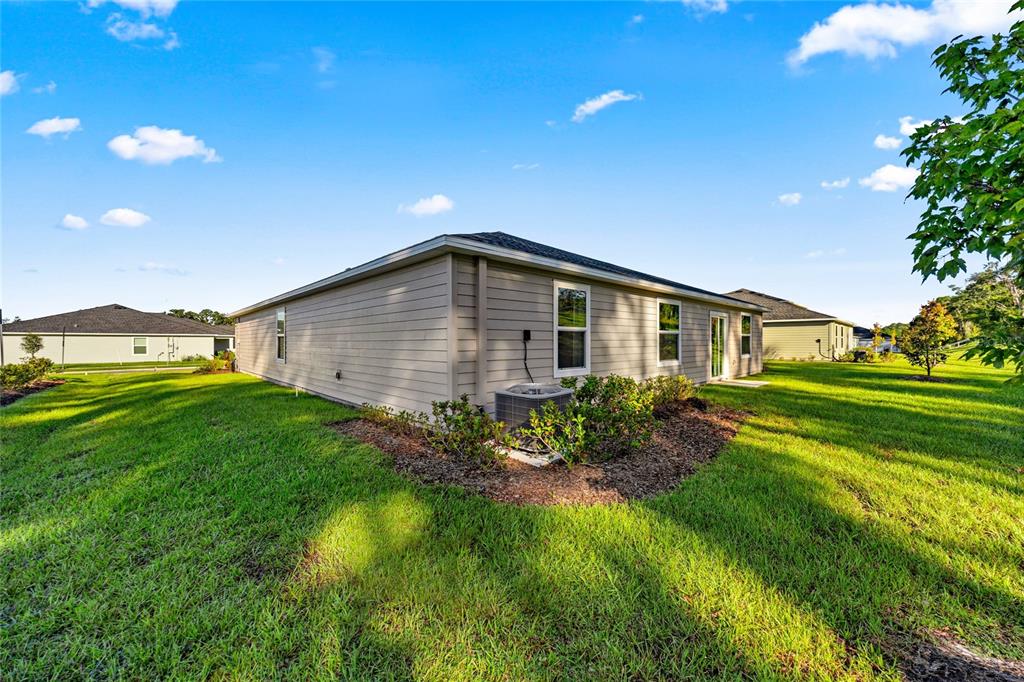 The exterior of a beige, single-story house features a lawn, landscaping, and an air conditioner — 8059 SW 45TH COURT, OCALA, FL