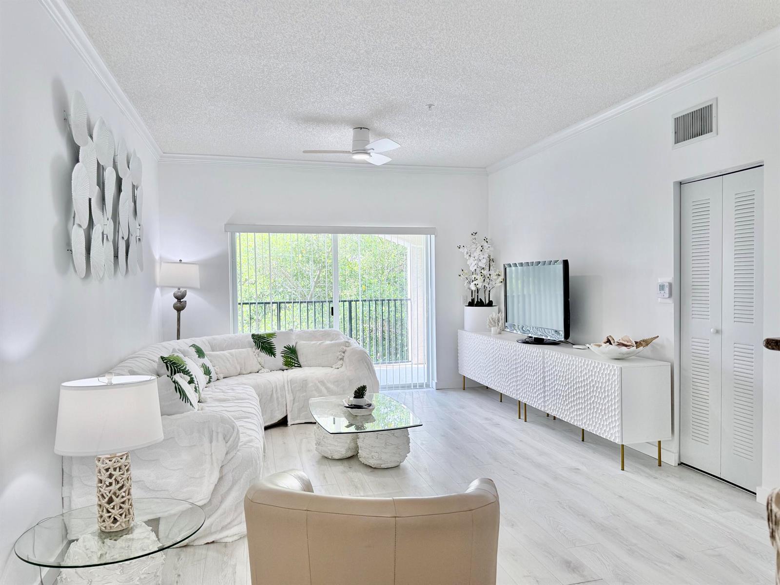 A bright living room features white furniture, a glass coffee table, and a sliding glass door — 4404 Tuscany Way # 4404, Boynton Beach FL 33435, BOYNTON BEACH, FL