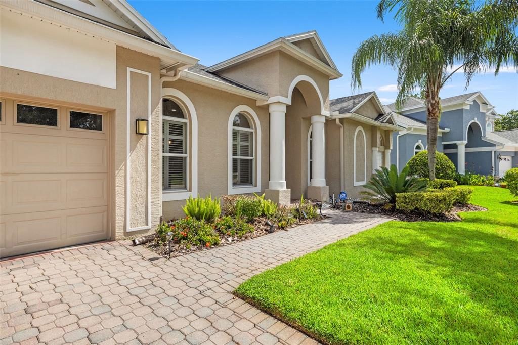 A tan stucco house features a paved driveway, arched windows, and a covered entryway — 17308 CHENANGO LANE, TAMPA, FL