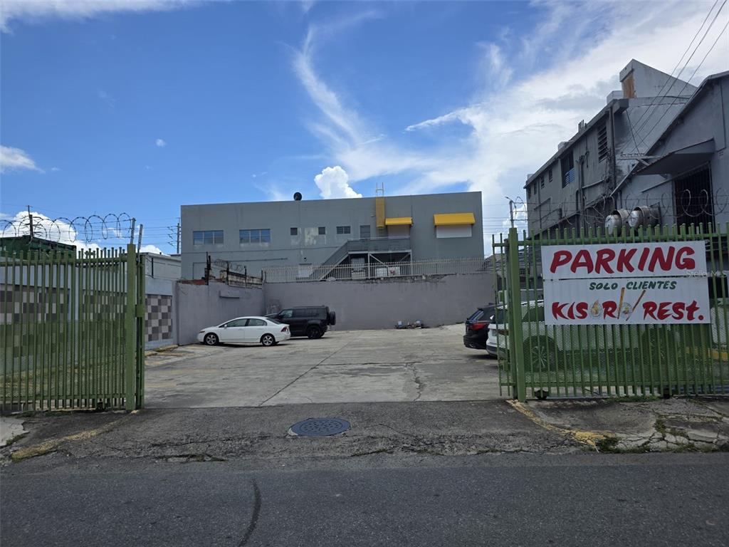 A paved parking lot is enclosed by a green metal fence with a parking sign — 1260 CORNER CORCHADO ST., SANTURCE WARD, SAN JUAN, PR