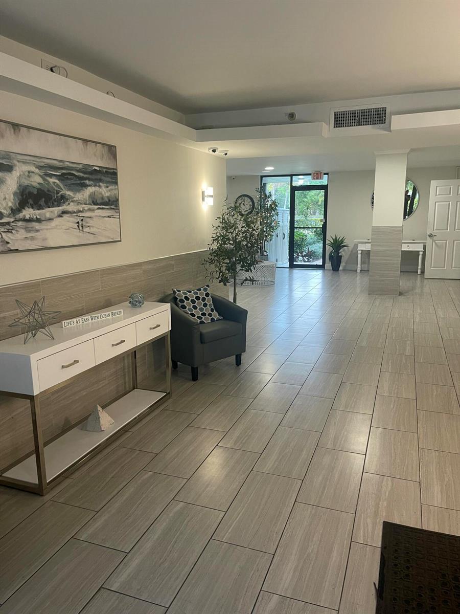 A modern lobby features light wood-look tile flooring, a white console table, and a gray armchair — 955 Egret Circle # 411, Delray Beach FL 33444, DELRAY BEACH, FL