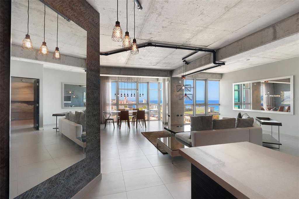 A modern living and dining area with concrete ceilings, industrial lighting, and floor-to-ceiling ocean views — 404 DE LA CONSTITUCION AVENUE UNIT 708, SAN JUAN, PR