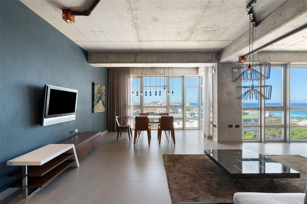 A modern living and dining area features concrete ceilings, a blue accent wall, and ocean views — 404 DE LA CONSTITUCION AVENUE UNIT 708, SAN JUAN, PR