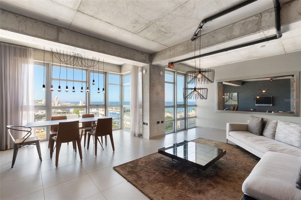 A modern open-concept living and dining area features concrete ceilings, floor-to-ceiling windows, and ocean views — 404 DE LA CONSTITUCION AVENUE UNIT 708, SAN JUAN, PR