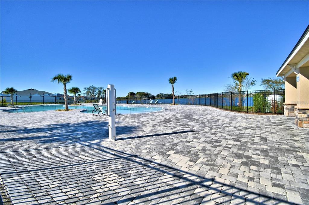 A paved pool deck features a shower station, palm trees, and a view of a lake — 1734 CARNOSTIE ROAD, WINTER HAVEN, FL
