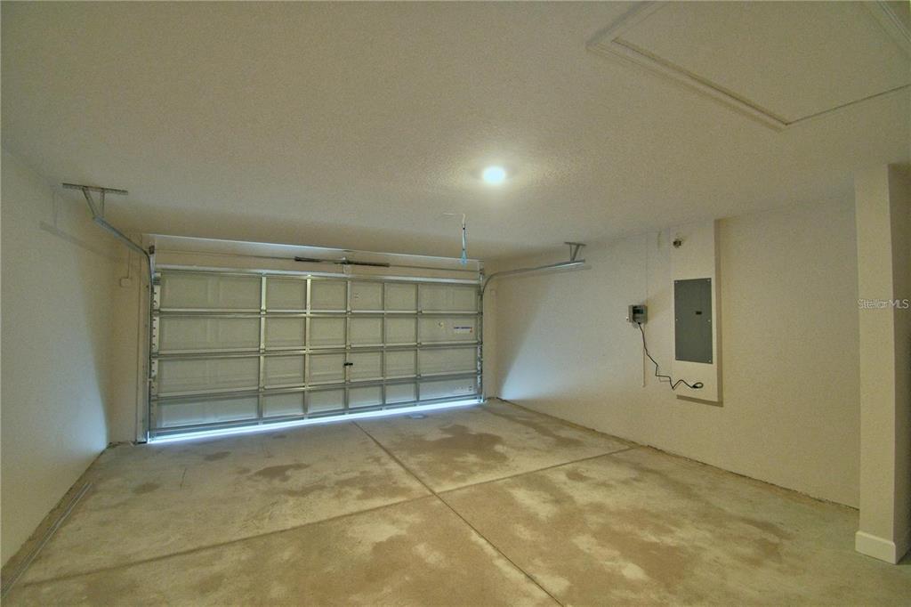 An empty garage features a white sectional door, concrete flooring, and a wall-mounted electrical panel — 1734 CARNOSTIE ROAD, WINTER HAVEN, FL
