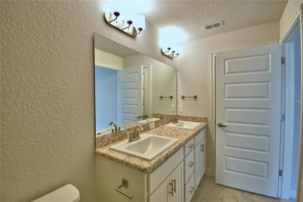 A bathroom features a double vanity with a granite countertop, white cabinets, and a large mirror — 1734 CARNOSTIE ROAD, WINTER HAVEN, FL