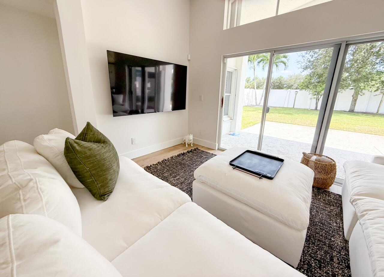 A living room features a white sectional sofa, a large ottoman, and a wall-mounted television — 7895 Manor Forest Boulevard, Boynton Beach FL 33436, BOYNTON BEACH, FL