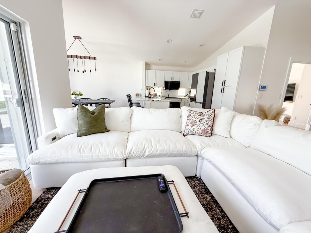 A bright living room features a large white sectional sofa facing an open-concept kitchen — 7895 Manor Forest Boulevard, Boynton Beach FL 33436, BOYNTON BEACH, FL