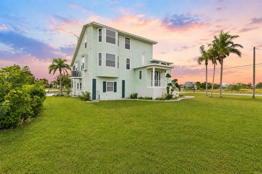 A three-story light green house with a porch stands on a grassy lawn at sunset — 3302 TURKS CAP DRIVE, HERNANDO BEACH, FL