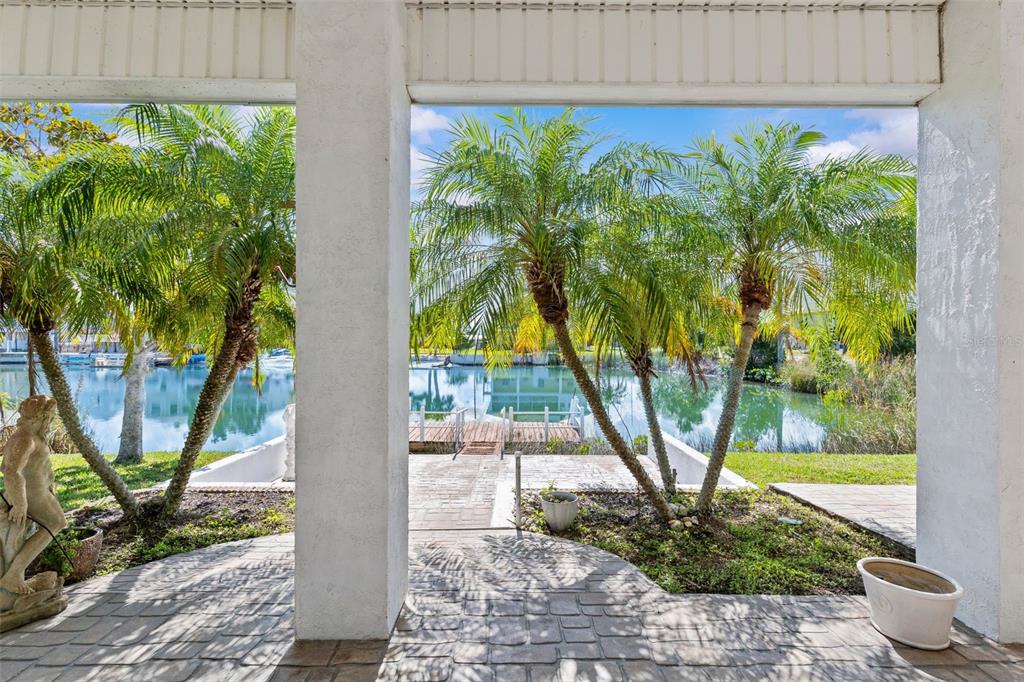 A covered patio overlooks a canal with palm trees, a dock, and a stone walkway — 3302 TURKS CAP DRIVE, HERNANDO BEACH, FL