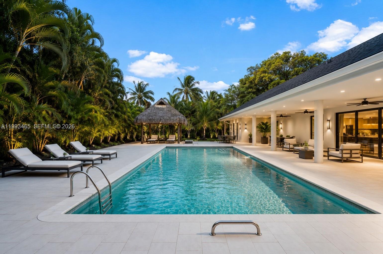 A rectangular swimming pool sits on a patio next to a house with a covered porch — 7997 SW 76th Avenue, Miami FL 33143, MIAMI, FL