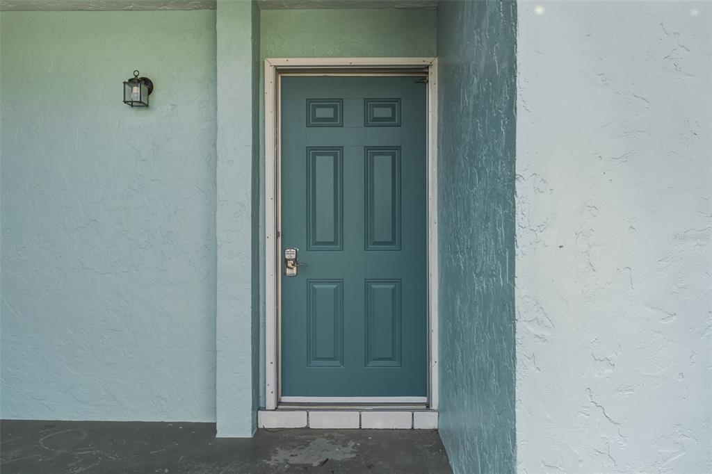 A teal front door with a keypad lock is set into a light blue exterior wall — 5055 N BEACH ROAD UNIT 108, ENGLEWOOD, FL