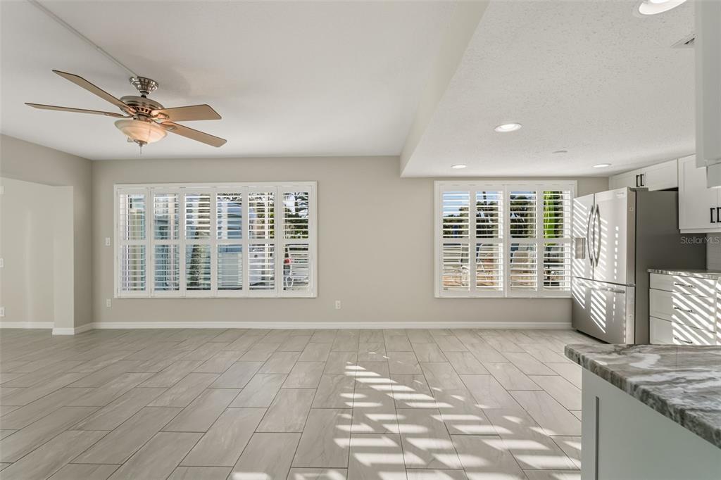 A bright, open-concept room features light gray tile flooring, white plantation shutters, and a ceiling fan — 5055 N BEACH ROAD UNIT 108, ENGLEWOOD, FL